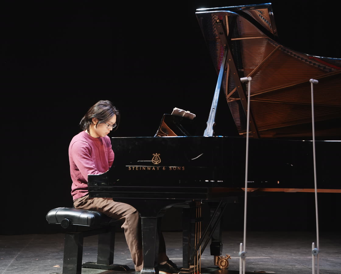 A member performing on a Steinway grand under stage lights